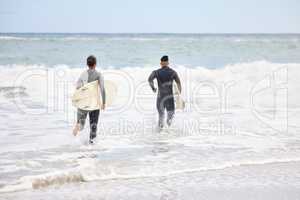 We belong in the ocean. Shot of an unrecognizable couple running into the water with surfboards at the beach.