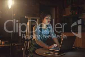 Working around the clock to maintain her business. Shot of a young entrepreneur working late on a laptop in a workshop.