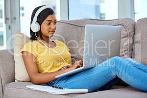 Downloading all my favourite tracks. Shot of a teenage girl listening to music and using a laptop at home.