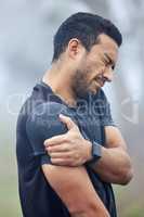 This pain is becoming more unbearable by the minute. Shot of a sporty young man holding his shoulder in pain while exercising outdoors.