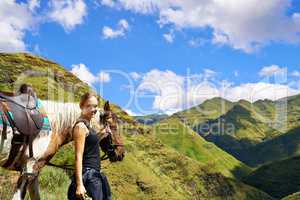 On top of the world. A young woman with her horse on a mountain trek.