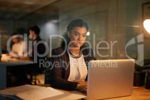 Burning the midnight oil. Shot of a young businesswoman using her laptop while working overtime in the office.