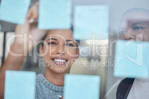 Hard work helps a business make progress with profits. Shot of two businesspeople brainstorming with notes on a glass wall in an office.