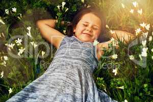 Making friends with the flowers. Shot of a cute little girl lying in a field of wildflowers outside.