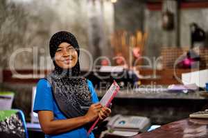 Youre always welcome here. Portrait of a smiling muslim thai woman standing behind a hotel reception desk holding a clipboard.