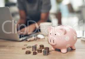 Saving allows you to enjoy greater financial security. Closeup shot of coins and a piggybank on a table with an unrecognisable businesswoman working in the background.