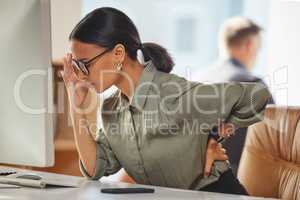 The aches and pains of a stressful day. Shot of a young businesswoman experiencing back pain while working in an office.