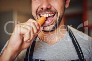 Hes got a carotene craving. Cropped shot of an unidentifiable young man eating a carrot in his kitchen at home.