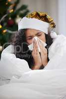 Shes got a case of the Christmas sniffles. Cropped shot of an attractive young woman blowing her nose while wearing a Christmas hat and lying on the sofa at home.