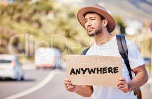 Travelling is hard. Shot of a young man holding a sign that reads anywhere while hitchhiking on the side of the road.