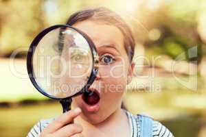 Curious about the world. Portrait of a little girl looking through a magnifying glass in amazement.
