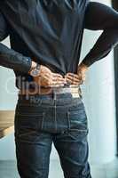 His back muscles are getting tense and tight. Shot of a young businessman suffering from back pain while working in an office.