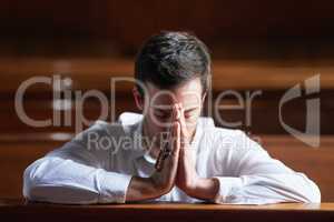 His faith is stronger than his fear. Shot of a young man praying in a church.