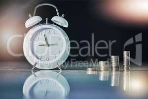 Investments and returns take time. Shot of an alarm clock and coins on a desk in an empty office.