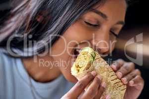 Ive never been so hungry in my life. Shot of a young woman enjoying a wrap during lunch.