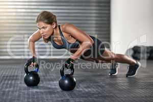 Upper body strength. Full length shot of a young woman working out with kettle bells at the gym.