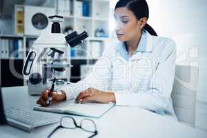 She studied hard, she got far. Shot of a young scientist writing notes while conducting medical research in a laboratory.