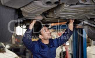 Could be the undercarriage.... Cropped shot of a handsome young male mechanic working on the engine of a car during a service.