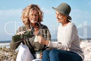 Can I top you up. Cropped shot of two attractive mature women enjoying some coffee while sitting on the beach.