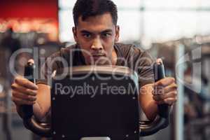 Ridding my way to some tight calves. Shot of a young man using an exercise bike in the gym.
