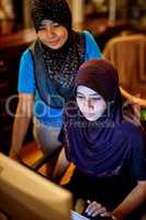 Checking the online reservations at hotel reception. Shot of two muslim thai women working on a computer at a hotel reception desk.