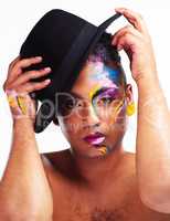 Le me fix my crown real quick. Portrait of a gender fluid young man wearing face paint and a hat posing against a white background.
