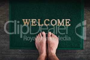 Home is where you can kick off your shoes. High angle shot of a mans bare feet standing on a welcome mat.