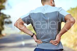 Take it one day at a time. Rearview shot of an unrecognisable man holding his lower back in pain while exercising outdoors.