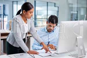 I need you to read over this. Shot of an attractive young businesswoman standing and getting her intern agent to sign his contract in the office.