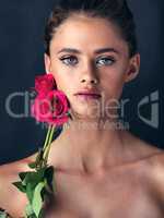 Two natural beauties in their element. Studio shot of an attractive young woman posing next to a couple of beautiful pink roses.