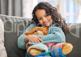 Comfort in a toy. Shot of an adorable little girl sitting alone on the sofa at home and holding a teddy bear.