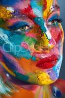 Stay colourful. Studio shot of a young woman posing with multi-coloured paint on her face.