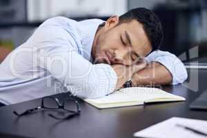 I just need a few minutes. Shot of an exhausted businessman having a quick nap on the desk at work.