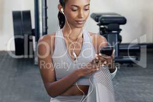 Compiling a playlist of the best tracks for her workout. Shot of a sporty young woman using a cellphone and wearing earphones in a gym.