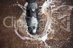 Be careful not to fall. Shot of a unrecognizable man walking in a puddle of water outside.