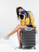 Im taking the necessary precautions to protect myself while traveling. Shot of a young woman wearing a mask while sitting on her suitcase.