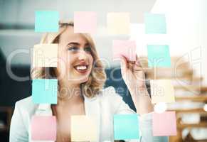 Generating genius ideas. Shot of a businesswoman arranging sticky notes on a glass wall in a modern office.