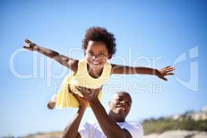 Helping his daughter soar. A father lifting his adorable daughter into the air while enjoying a day at the beach.