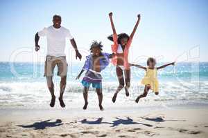 Woohoo Vacation time rocks. An excited african american family jumping into the air on the beach with a beautiful ocean in the background.