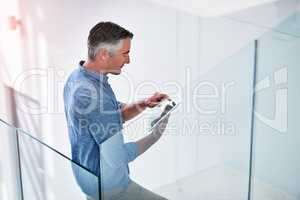 Keeping up with the pace of modern business. Shot of a mature businessman using a digital tablet on the stairs in a modern office.