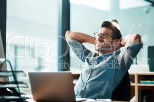 Beating the deadline like the champ he is. Shot of a young businessman taking a break at his desk in a modern office.