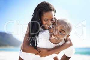 Surprise, my love. A handsome african-american man giving his girlfriend a piggyback on the beach.