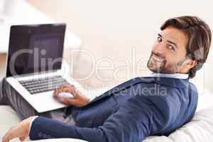 Work satisfaction guaranteed. An attractive businessman reclining on the couch while working on his laptop.