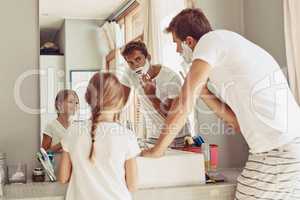 Its so much fun to watch daddy shave. Shot of a happy little girl watching her father as her shaves by the sink.