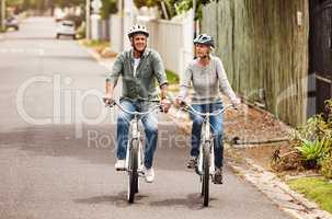 This was a good idea. Shot of a cheerful senior couple riding on bicycles together outside in a suburb.