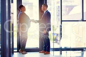 Mergers help to enhance the value of business. Shot of two businesspeople shaking hands in an office.