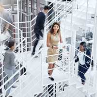 Shes a calm amongst the office storm. Portrait of a young professional standing on a stairs with colleagues rushing around her.