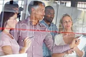 Clearly communicating his ideas. A group of business colleagues brainstorming together at a glass wall.