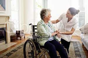 Helping others is a calling. Shot of a smiling caregiver helping a senior woman in a wheelchair at home.