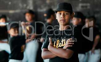 My mom says that Im pretty good. Portrait of a young baseball player standing with his arms crossed with his teammates standing in the background.